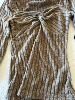 Beige ribbad omlottklänning - Säljer en beige långärmad klänning med ribbad struktur och omlottdetalj framtill. Klänningen har en mjuk, stickad känsla och är perfekt för dig som gillar en avslappnad men ändå snygg stil. Passar bra till både boots och sneakers.