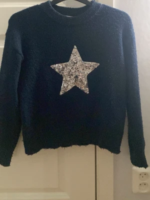 Mörkblå stickad tröja med paljettstjärna - Cool mörkblå stickad tröja från Gina Tricot med en stor silverfärgad paljettstjärna på bröstet. Tröjan har rund halsringning och långa ärmar. Perfekt för dig som gillar att sticka ut med glittriga detaljer och mjuka material.