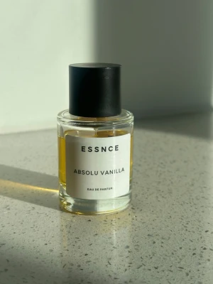 ESSNCE Absolu Vanilla Eau de Parfum - ESSNCE Absolu Vanilla Eau de Parfum i en stilren, rund glasflaska med svart lock. Doften har en varm, söt vaniljkaraktär och flaskan har en minimalistisk vit etikett med svart text. Perfekt för dig som gillar mjuka och krämiga doftnoter.