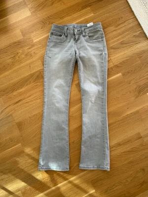 Ljusgrå bootcut jeans från LTB - Säljer ett par ljusgrå bootcut jeans från LTB med klassisk femficksdesign och bälteshällor. Jeansen har en knappgylf och är tillverkade i mjukt denimtyg med lite stretch för extra komfort. Perfekta för en avslappnad och trendig look.