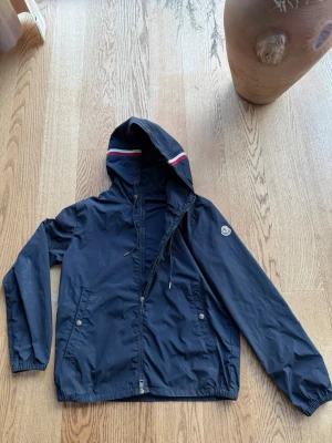 Mörkblå Moncler vindjacka  - Säljer nu min riktigt snygga Moncler vindjacka. Jackan är i bra skick, har bara några få defekter vid fickan. Priset är förhandlingsbart. Hör av dig vid fler frågor
