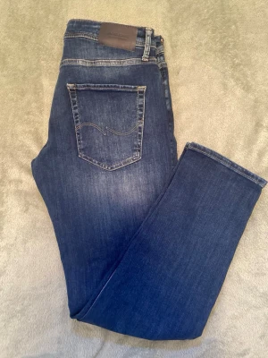 Helt nya jeans från J&J - Snygga mörkblå jeans från Jack & Jones med klassisk femficksmodell och diskret broderad bakficka. Jeansen har en smal passform och är tillverkade i mjuk, stretchig denim för extra komfort. Perfekta till en avslappnad stil.