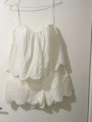 Vita broderade shorts med spetskant från H&M  - Säljer ett par vita shorts med broderade detaljer och vågig spetskant. Shortsen har en romantisk look med fina hålbroderier och är perfekta för varma dagar. Tillverkade i ett lätt och luftigt material som känns skönt mot huden.