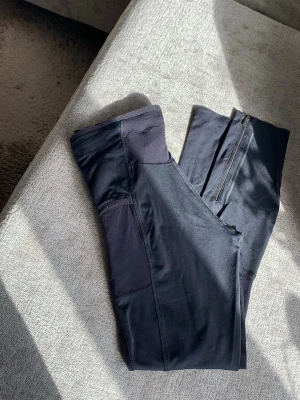 Svarta träningsleggings Peak Performance - Snygga svarta träningstights från Peak Performance med dragsko i midjan, praktiska sidfickor och en liten midjeficka för nycklar eller AirPods. Tillverkade i stretchigt funktionsmaterial som andas, perfekta för gymmet eller löprundan. Diskret logga på snörena och smidig passform. En reflex har nötts bort (se sissta bild), övrigt i mycket gott skick. 