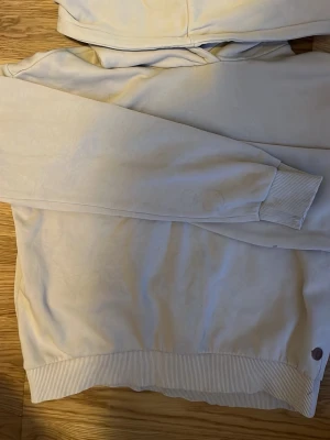 Beige hoodie med huva - Säljer en beige hoodie från Ü (KappAhl) med ganska stor huva och ribbade muddar vid ärmslut och nederkant. Hoodien är tunn, men varm, och har en enkel, stilren design utan tryck eller mönster (förutom märket där nere). Perfekt för dig som gillar basic mindre hoodies och något som är enkelt att styla. Storleken är 146/152 men jag är ca 175 och den passar väldigt bra💞💞