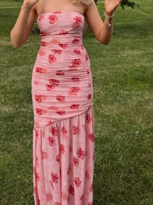 ADOORE Rosa blommig långklänning omlott - Säljer en rosa långklänning med blommigt mönster i rött och rosa. Klänningen är axelbandslös, har omlottdetalj och smickrande rynkningar upptill. Perfekt för bal och sommarens alla tillfällen! 