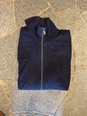 Mörkblå ziptröja i 100% kahsmir  - Mörkblå tröja i 100% kahsmir, den har en hel dragkedja framtill och hög krage. Passar perfekt för lager på lager. Som man ser på bilderna så är de hål i båda armhålorna, samt ett i slutet av armen. Dessa ser man dock inte vid användning (kan skicka bild med den på om du vill). Nypris runt 2449, mitt pris: 749