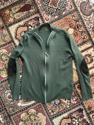 Stenströms  zip-up Merinoull - Snygg olivgrön stickad tröja från Stenströms i 100% merinoull. Tröjan har hel dragkedja framtill och mörka mockadetaljer på armbågarna. Perfekt för dig som gillar klassisk stil. Ribbstickade muddar vid ärmslut och nederkant.