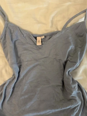 Ljusblå linnetopp från nelly - Söt ljusblå linnetopp från nelly med smala axelband och v-ringad hals. Toppen har en enkel design med en liten spetskant vid urringningen. Perfekt för varma dagar och enkel att matcha med jeans eller kjol.