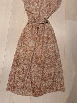 Beige långkjol med mönster och snörning - Långkjol i möstrat tyg. Kjolen har en avslappnad passform och justerbar midja med snörning. 