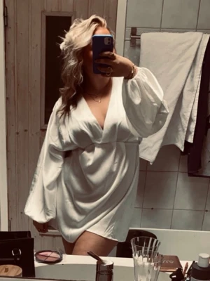 Vit omlottklänning med ballongärmar - Snygg vit kort omlottklänning med ballongärmar och knyt i midjan. Klänningen har v-ringning och är tillverkad i siden som ger en lyxig känsla. Perfekt för student eller skolavslutning🥹❤️