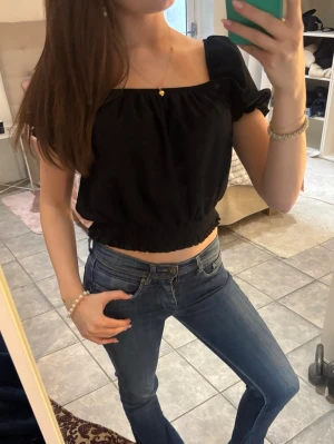 Svart croppad topp med puffärm - Säljer en svart croppad topp med puffärmar och fyrkantig ringning. Toppen har resår i midjan och vid ärmsluten för en snygg passform. Perfekt till jeans eller kjol för en trendig look.