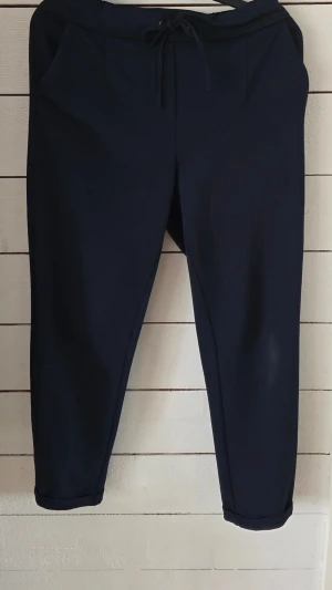 Mörkblå byxor Vero Moda - Mörkblå byxor från Vero Moda med dragsko i midjan och två sidofickor. Byxorna har en avslappnad passform och är gjorda i ett mjukt, stretchigt material som känns skönt mot huden.