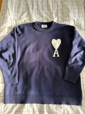 Ami navy stickad tröja - Mörkblå stickad tröja från Ami med rund halsringning och ribbade muddar. På bröstet finns ett vitt hjärta och bokstaven A som är typiskt för Ami. Tröjan är gjord i mjukt stickat material och har en avslappnad passform. Storlek XL och i bra skick. Hör gärna av er om ni har några frågor eller bud!