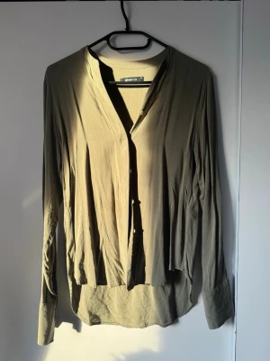 Beige långärmad skjorta Gina Tricot - Stilren beige skjorta från Gina Tricot med v-ringning och knappar framtill. Skjortan har långa ärmar och en avslappnad passform, perfekt för en trendig och enkel look. Tillverkad i mjukt material som känns skönt mot huden.