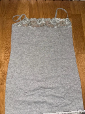 Grå linnetopp med spetsdetalj - Snygg grå linnetopp med tunna axelband och spets upptill. Toppen har en enkel och stilren design med en feminin touch tack vare spetsen. Perfekt att matcha med jeans eller kjol för en trendig look.