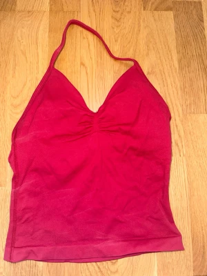 Röd halterneck linne - Snygg röd linnetopp med halterneck och v-ringad front. Toppen är ärmlös och har en lätt rynkning vid bysten för extra detalj. Perfekt för varma dagar och enkel att styla till olika looks.