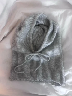 Grå ribbstickad balaclava med knytband - Mysig grå balaclava i ribbstickat med knytband framtill. Vet inte märke tyvärr, köpt på vinted. Har klippt där nere, men syns inte när man har på sig den. Annars fint skick!!💕💕💕