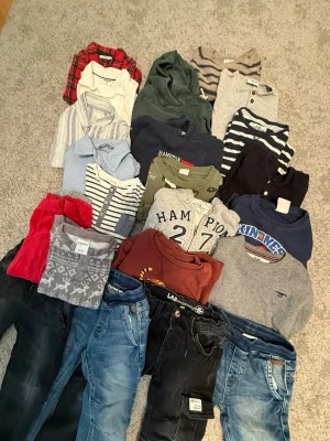 Stort klädpaket med tröjor och byxor - Säljer ett blandat klädpaket för barn, med flera långärmade tröjor, skjortor och jeans i olika färger som rött, grönt, blått, grått och randigt. Inkluderar märken som Hampton Republic och LAB Industries. Perfekt för dig som vill ha en varierad garderob med både mönstrat och enfärgat.