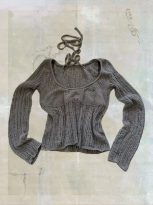 Grå ribbstickad topp med halterneck - Trendig grå ribbstickad topp med lång ärm och unik halterneck-detalj. Figurnära passform och croppad längd ger en modern look. Perfekt för dig som vill ha något extra till garderoben.