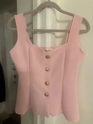 Ljusrosa topp med guldknappar från Zara - Säljer en ljusrosa topp med breda axelband och snygg figurnära passform. Toppen har dekorativa guldknappar framtill och är sydd i ett slätt, något tjockare tyg som ger struktur. Perfekt för dig som gillar en chic och trendig look.