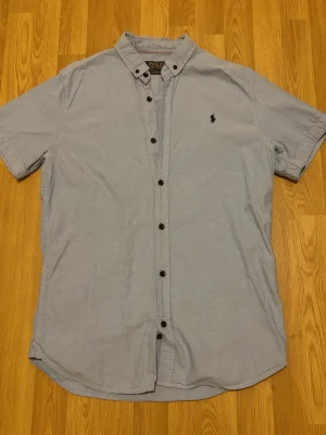 Ljusblå kortärmad skjorta Polo Ralph Lauren - Säljer en ljusblå kortärmad skjorta från Polo Ralph Lauren i bomull. Skjortan har klassisk krage, knappar framtill och den ikoniska loggan broderad på bröstet. Perfekt till sommaren och enkel att styla med jeans eller shorts.