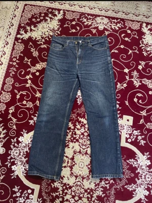 Mörkblå Jeansbyxor - Säljer ett par klassiska mörkblå jeans med raka ben och snygga kontrastsömmar i gult. Jeansen har fem fickor, bälteshällor och stängs med dragkedja och knapp. Mindre skavanker syns i sista bilden. Det står att den är i storlek L, men den skulle nog passa en strl M mer. 100% bomull. 2 för 120 kr på alla herrbyxor. 