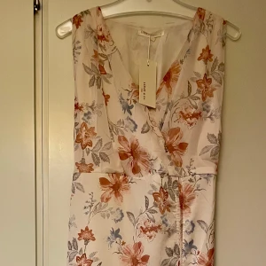 Blommig klänning från Lovie & Co i stl 40/L - Ny med lapp. ”Typha dress” stl 40/L.  Väldigt tunt svalt material, lätt fodrad. Ljusbeige/naturfärgad blommig med möjlighet att snöra till mer figurformad. Uppskattar att den sitter bäst på en 38/40. 