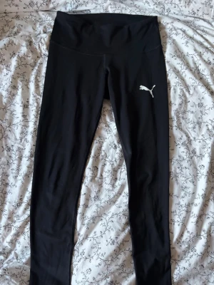 Svarta träningstights från Puma - Snygga och stretchiga svarta leggings från Puma med medelhög midja och klassisk logga på låret. Tillverkade i stretchigt material som sitter skönt och följer kroppen. Perfekta för träning, gymmet eller gympan. Enkel och stilren design som passar till det mesta. Innerbenslängd: 65cm Den har några fiber på sig från tennisbollar men kan enkelt fixas med en pincett och lite tålamod fler mått eller funderingar? Tveka inte och fråga! Pris kan såklart diskuteras 💗
