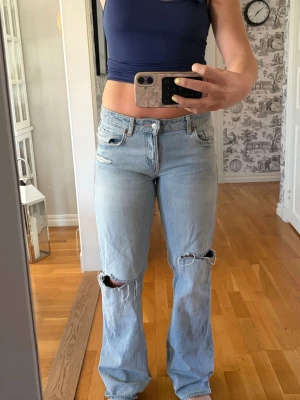 Ljusblå zara jeans - Säljer ett par ljusblå jeans med raka/vida ben och  hål vid knäna. Jeansen har klassisk femficksmodell, medel hög midja och slitna detaljer för en trendig look. Perfekta för dig som gillar en avslappnad och cool stil. Är från Zara och endast använda några gånger i storlek 38
