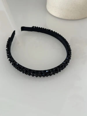 Svart diadem med glittrande stenar - Snyggt svart diadem täckt med glittrande svarta stenar som ger en lyxig och trendig känsla. Diademet har en klassisk form och är perfekt för att lyfta vilken outfit som helst. Nypris 100. Pris kan diskuteras.