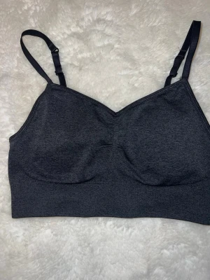 Mörkgrå sport-bh - Mörkgrå sport-bh med justerbara axelband. Den har en ribbad nederkant och rynkad detalj framtill. Från hm , storlek s, mycket bra skick!