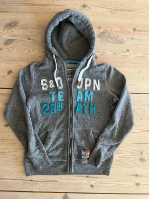 Superdry Hoodie - Säljer en grå vintage hoodie från Superdry med dragkedja och huva med vita snören. Det är storlek M och är normal i storleken. Perfekt för alla stilar! Hör gärna av er vid frågor!🙌🙌
