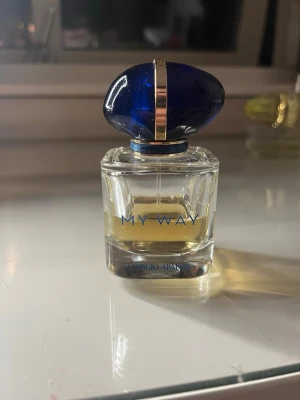 Giorgio Armani My Way parfym - En elegant parfymflaska från Giorgio Armani, modellen My Way. Flaskan är genomskinlig med blå text och har ett lyxigt blått och guldigt lock. Innehållet är ljusgult och flaskan har en stilren, modern design som känns exklusiv.