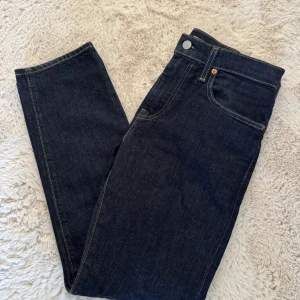 Mörkblå raka jeans från Levi's - Snygga mörkblå jeans från Levi's med raka ben och klassiska kontrastsömmar. Femficksmodell med silverfärgade och kopparfärgade nitar. Tillverkade i slitstark denim med en tidlös look som passar till det mesta.