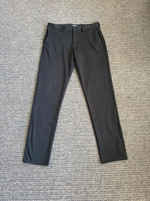 Chinos - Snygga svarta kostymbyxor från Jack & Jones i slim fit-modell. Byxorna har klassiska fickor fram, bälteshällor och stängs med knapp och dragkedja. Perfekta för en clean och stilren look.