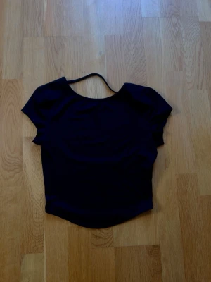Svart croppad topp med kort ärm - Svart topp som har rygglös. Ser blå ut på bilden men är svart i verkligheten. Har inte använt den men drog bort lappen utan att tänka💗