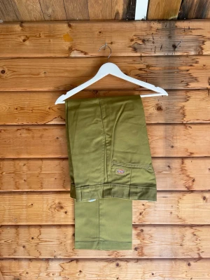 Olivgröna chinos från Dickies - Snygga olivgröna chinos från Dickies med klassisk rak passform. Tillverkade i ett slitstarkt bomullsmaterial. Perfekta för en avslappnad och trendig stil.