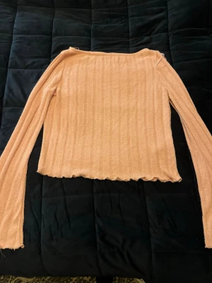 Ljusrosa ribbad långärmad tröja - Säljer en ljusrosa långärmad tröja med ribbad struktur och lätt vågig kant nedtill. Tröjan har en rak passform och är tillverkad i ett mjukt, stretchigt material. Perfekt för dig som gillar en enkel men söt stil.