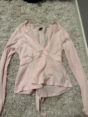 Ljusrosa omlottopp med knyt - Supersöt ljusrosa omlottopp med långa ärmar och en rosett som man knyter i ryggen. Från Gina Tricot💞 priset är diskuterbart