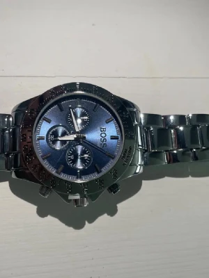 Hugo boss klocka  - En klocka från Hugo boss i silver med blått i använt ett par gånger bara. Har bytt batteri nyligen och lämnats in på service för att kolla så allt stämmer med den. Den är helt fel fri. Skriv vid frågor!!