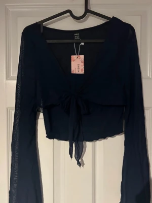 Mörkblå topp - Trendig mörkblå topp med långa, transparenta ärmar och snygg knytning framtill. Lätt V-ringning och tunt, flowy material som ger en luftig och feminin känsla. Perfekt för att lyfta din outfit både till vardag och fest.(ifrån shein) 