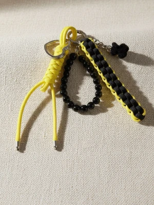 Handgjord Väskcharm & Nyckelring – Gul / Svart Paracord - Ge din väska eller dina nycklar en färgklick med denna handgjorda accessoar! Tillverkad i en snygg kombination av gult och svart slitstarkt paracord-snöre. Denna väskcharm/nyckelring är både praktisk och en cool detalj. • Färg: Gul och svart med matchande pärlor. • Användning: Passar perfekt som dekoration på väskan, ryggsäcken eller till nycklarna. • Skick: Ny / Handgjord. En unik detalj som sticker ut! Kika gärna på mina andra annonser för fler färgkombinationer. 