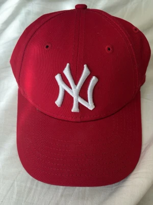 Röd  keps - Snygg röd keps.  Kepsen har böjd skärm och justerbar baksida. Tillverkad i bomullstyg som känns både slitstarkt och bekvämt. Perfekt för dig som vill ha en sportig och trendig look.