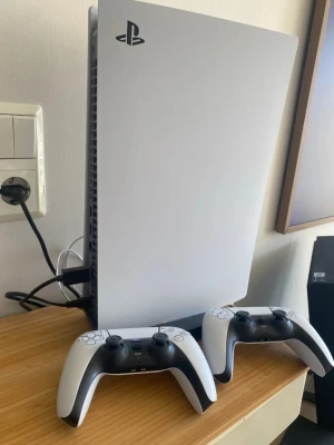 PlayStation 5 med två DualSense-kontroller - Säljer en PlayStation 5 från Sony i vit och svart design. Konsolen har en futuristisk, stilren form och medföljer två matchande DualSense-kontroller. Perfekt för gaming med vänner eller soloäventyr. Materialet är plast med matta och blanka ytor.