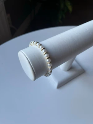 Vit och guldit armband  - Vit och guldit armband med elastiskt band så att det är lätt att ta på och av det är även handgjort.