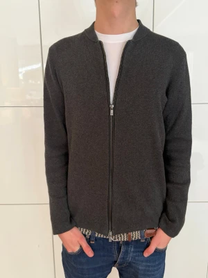 Massimo Dutti Mörkgrå ziptröja - Mörkgrå ziptröja med rak passform och hel dragkedja framtill. Tröjan har rund halsringning och är tillverkad i mjukt bomullsmaterial. Perfekt att slänga över en t-shirt för en clean och enkel look.