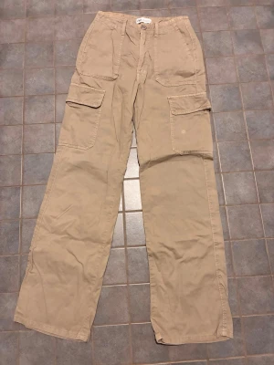 Beige cargobyxor från ZARA - Snygga beige cargobyxor från ZARA med raka ben och stora fickor på sidorna. Byxorna har klassisk cargomodell med knapp och dragkedja framtill samt praktiska fickor både fram och bak. Perfekta för en avslappnad och trendig stil.