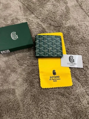 Grön plånbok och neccesär - Snygg grön plånbok från med det klassiska vita och svarta. Tillverkad i canvas med läderdetaljer. Kommer med . Perfekt för dig som gillar exklusiva accessoarer.