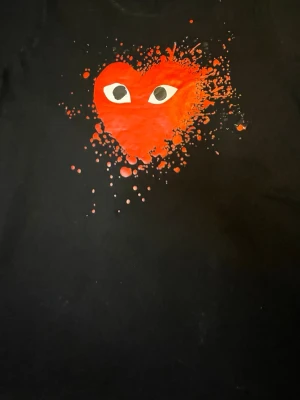 Svart CDG T-shirt, Comme des Garçons - Svart t-shirt från Comme des Garçons (CDG) med ikoniskt rött hjärta med ögon framtill ❤️  Sjukt clean men sticker ändå ut – passar perfekt till streetwear / y2k fits.  • Färg: Svart med rött tryck • Modell: Kortärmad t-shirt • Stil: Streetwear / minimal / trendy • Unisex • Bekväm och lätt att matcha  Perfekt basic med hype – funkar till allt 🔥
